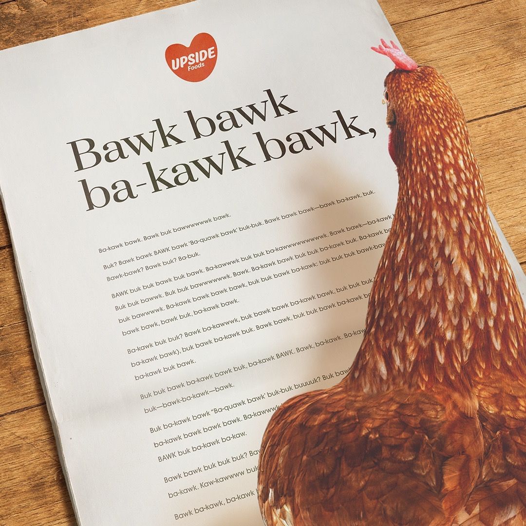 Upside Foods print ad with a chicken "reading" it